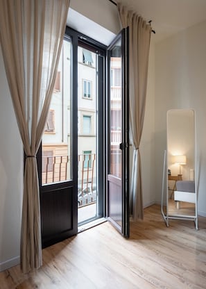 A room with a sliding glass door leading to a balcony, a bedside table with a lamp, and a mirror on the wall. - MusArt Yellow Room (Firenze)