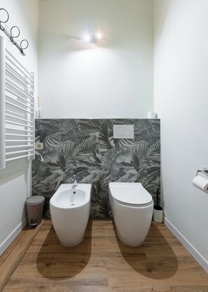 Une salle de bain avec deux toilettes, un bidet, un porte-serviettes et un support à papier toilette.