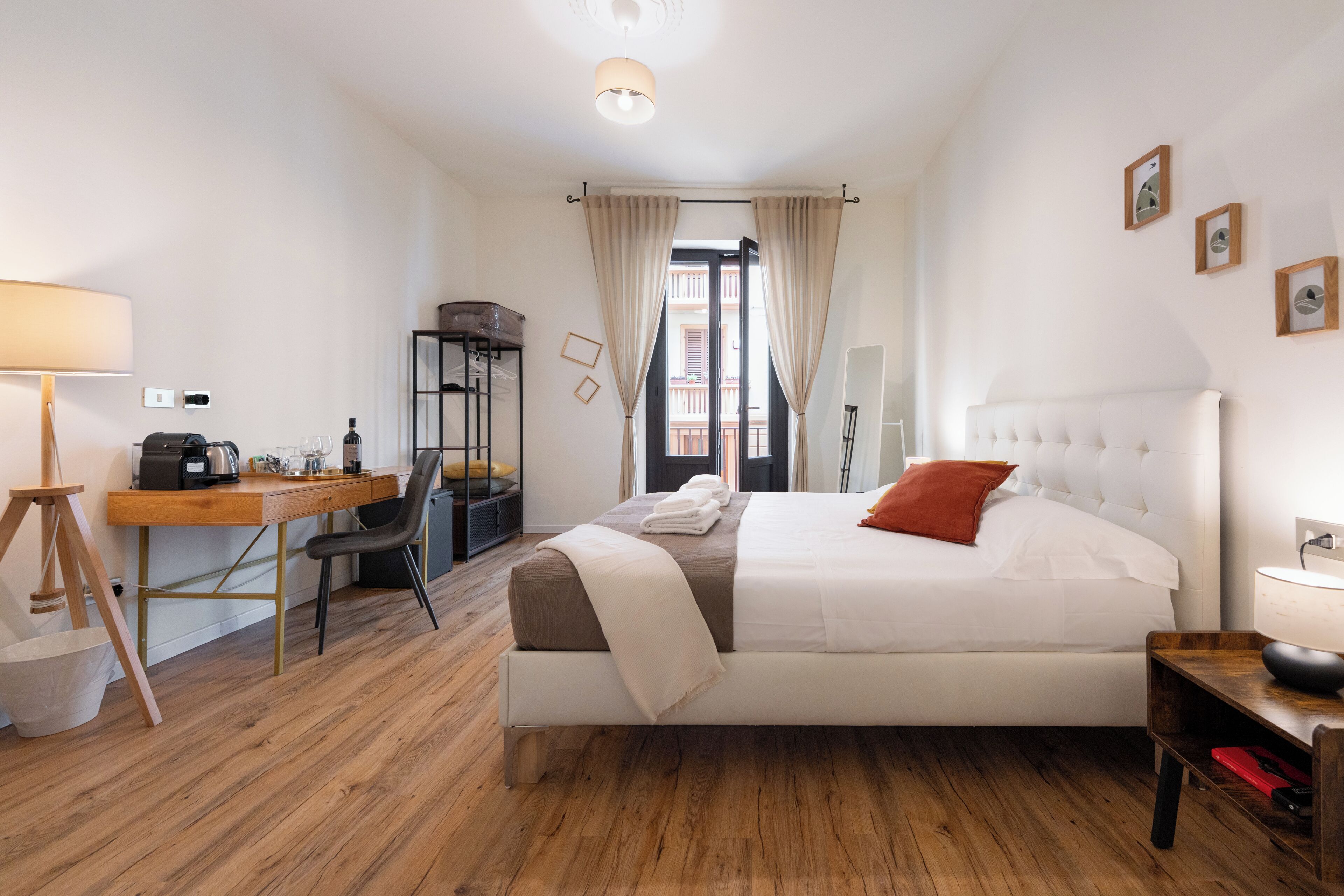 Ein Hotelzimmer mit einem Bett, einem Schreibtisch, einem Stuhl, einer Lampe, einem Bücherregal und einem Fenster mit Vorhängen.