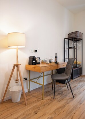 A compact room with a wooden desk, a chair, a lamp, a coffee maker, and a storage unit with shelves. - MusArt Yellow Room (Firenze)