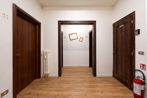 A hallway with wooden flooring, numbered doors, and a fire extinguisher. - MusArt Yellow Room (Firenze)