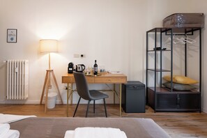 A hotel room with a bed, a desk with a chair, a lamp, a kettle, wine glasses, and a wardrobe. - MusArt Yellow Room (Firenze)
