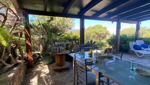 An outdoor dining area with a glass table, chairs, and a wooden side table. - Relaxing Home Near the Best Beaches of Stintino (Stintino)