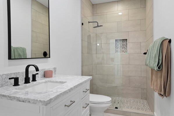 A modern bathroom with a glass-enclosed shower, a white sink with a marble countertop, and a toilet. - Lake Hartwell Escape (Westminster)