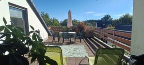 A terrace with a table and chairs, a potted plant, and a view of the surrounding area.