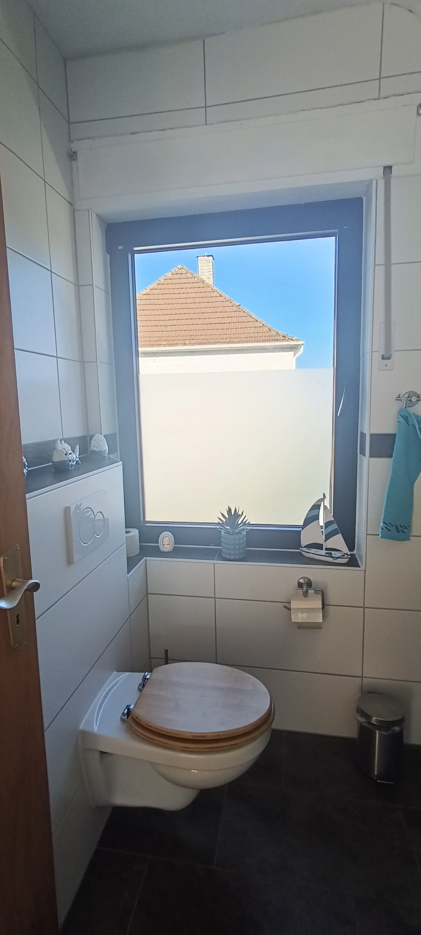 A bathroom with a toilet, a window, and a view of a building outside.