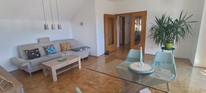 A living room with a sofa, coffee table, and a glass table with chairs. There is a door leading to another room and a potted plant. - Cozy vacation apartment with large roof terrace in an upscale residential area. (Halver)