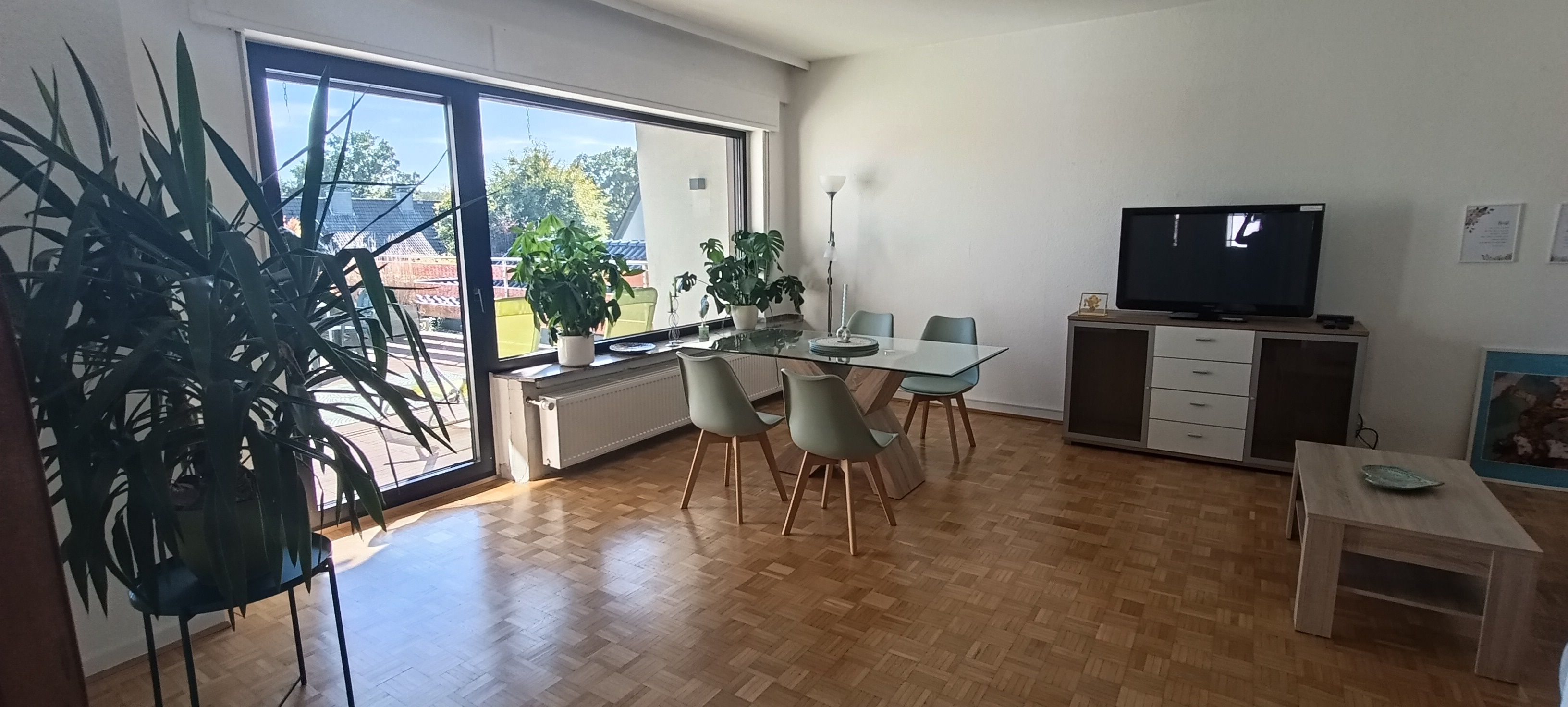En moderne stue med spiseplads, store vinduer og et fladskærms-tv.