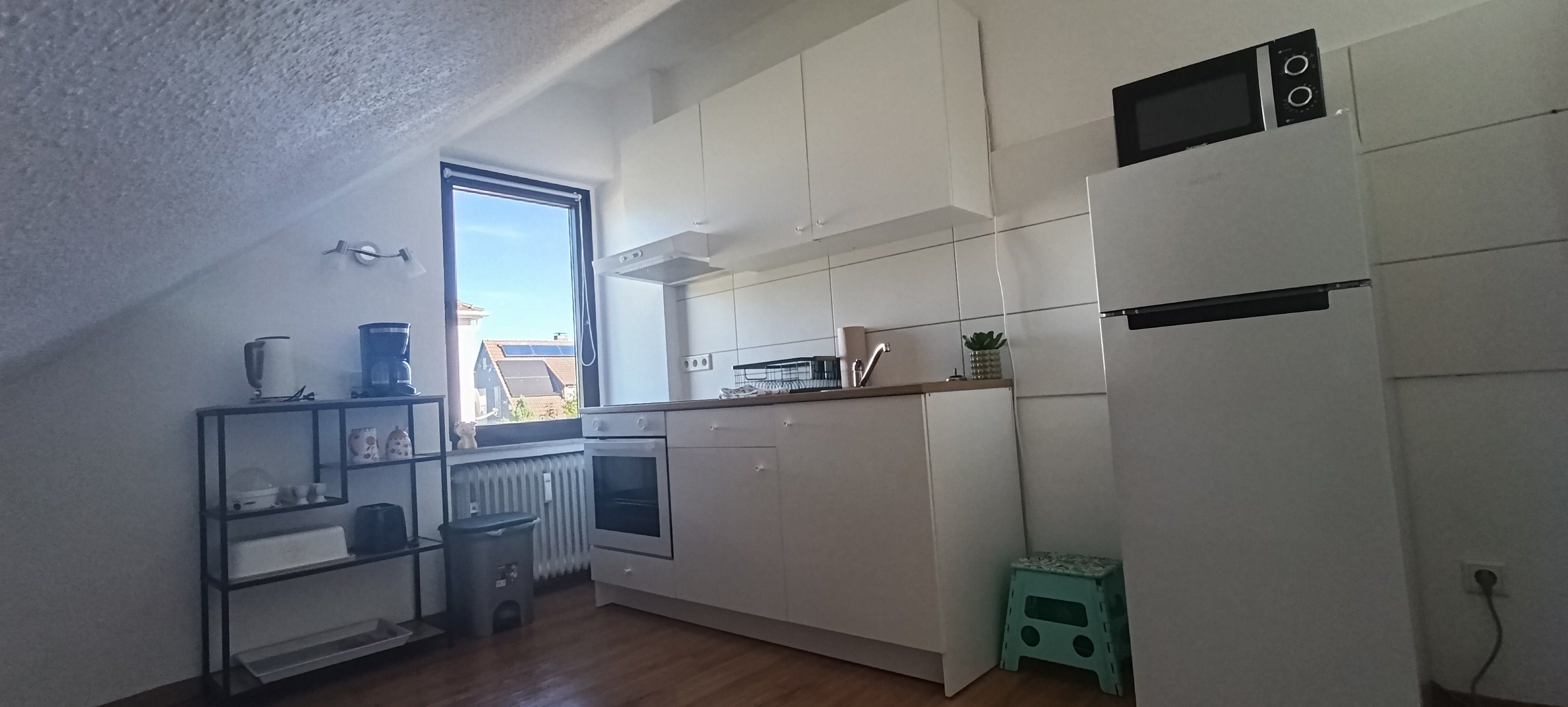 Una cucina compatta con mobili bianchi, forno integrato, microonde e una finestra con vista esterna.