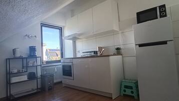 Una cucina compatta con mobili bianchi, forno integrato, microonde e una finestra con vista esterna.