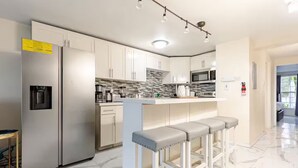 A modern kitchen with a stainless steel refrigerator, a built-in microwave, and a bar area with stools.