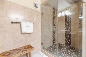 Een moderne badkamer met een douchecabine van glas, beige tegels, een houten bankje en een handdoekrek.