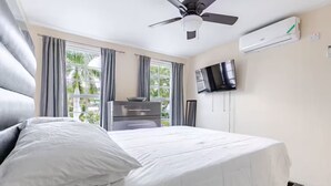 A hotel room with a large bed, a ceiling fan, a flat-screen TV, and an air conditioning unit.