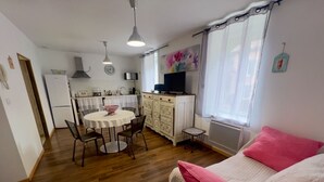 Un espace de vie compact comprenant un coin repas, une kitchenette et un lit agrémenté d’oreillers roses.