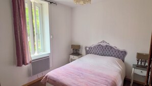 Une chambre à coucher avec un grand lit, deux tables de chevet, une fenêtre avec des rideaux et un luminaire au plafond.