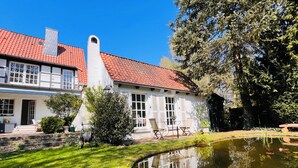 Edifici blanc amb teulada vermella, estany amb flors grogues i gespa ben cuidada.
