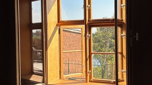 A room with a large, open window revealing a brick building and greenery outside. - Vacation apartment Fischerhaus Havelberg (Havelberg)