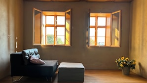 A room with two windows, a sofa, a small ottoman, and a potted plant. - Vacation apartment Fischerhaus Havelberg (Havelberg)