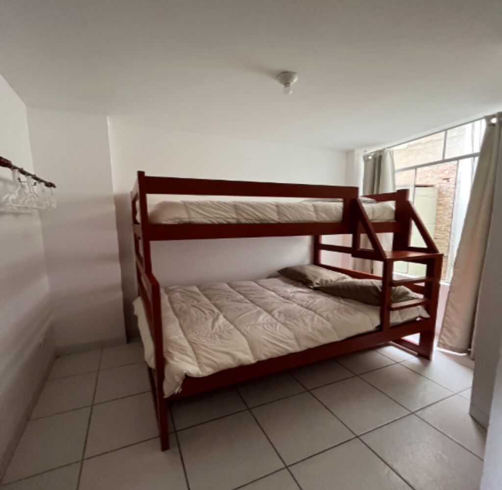 Una cama individual superpuesta en una habitación con suelo de baldosas y una ventana con cortinas.