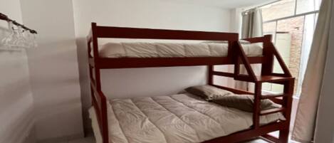 Una cama individual superpuesta en una habitación con suelo de baldosas y una ventana con cortinas.