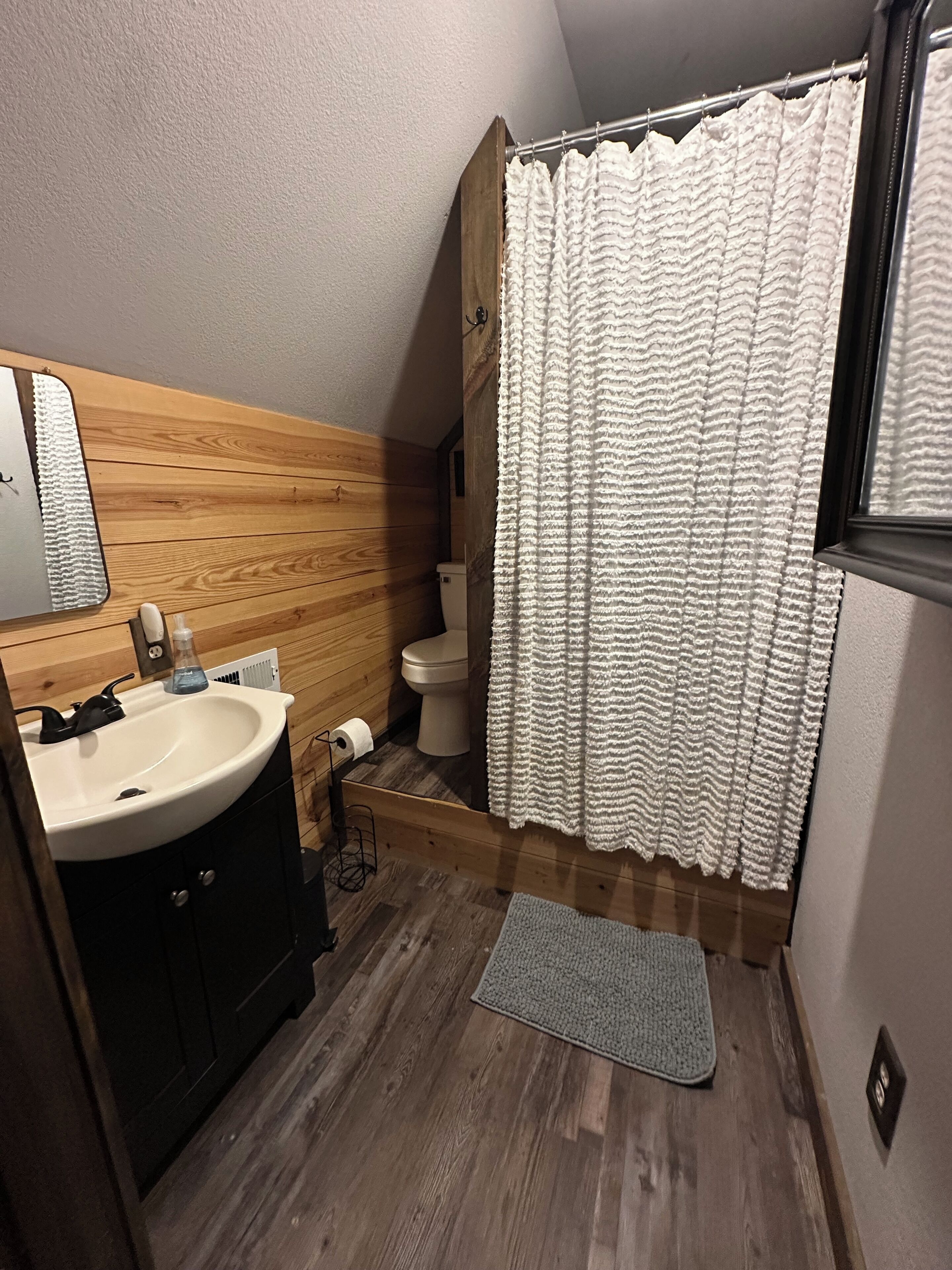 A bathroom with a wooden vanity, a sink, a toilet, and a shower curtain.