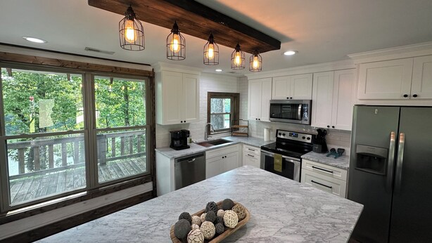 A modern kitchen with white cabinets, a marble countertop, a built-in oven, a microwave, and a stainless steel refrigerator.