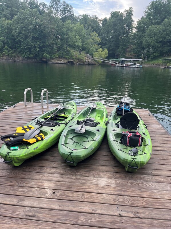 Three kayaks on a wooden dock with a calm lake and trees in the background.