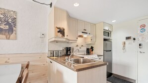 A modern kitchen with wooden cabinets, a stainless steel sink, a microwave, and a refrigerator. - LOFT de la montagne- MSA (Saint-Ferréol-les-Neiges)