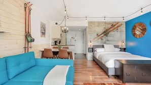A modern hotel room with a blue sofa, a bed, a wooden floor, and ski equipment on the wall. - LOFT de la montagne- MSA (Saint-Ferréol-les-Neiges)