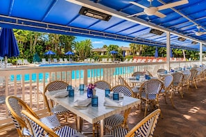 An outdoor pool area with lounge chairs and tables, a pool, and a covered seating area with umbrellas. - Park Shore Resort BLDG I #453-Great views (Naples)