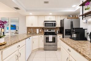 A modern kitchen with white cabinets, granite countertops, stainless steel appliances, and a coffee maker. - Park Shore Resort BLDG I #453-Great views (Naples)