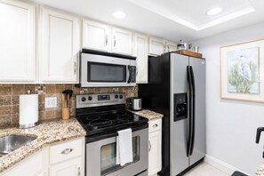 A kitchen with white cabinets, a stainless steel refrigerator, a microwave, and a stove.