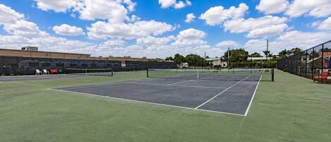 An outdoor tennis court with a net, green turf, and a clear sky.