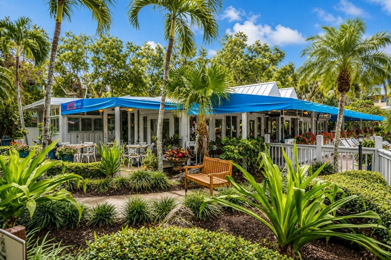 Een restaurant met terras, omgeven door palmbomen en tropische planten.