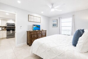 Ein Schlafzimmer mit Bett, Fernseher, Deckenventilator und Blick auf die Küche.