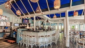 A spacious bar area with white bar stools, a central bar counter, and hanging pendant lights. - Park Shore Resort BLDG I #453-Great views (Naples)