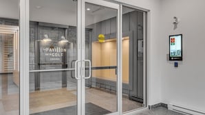 A modern hotel entrance with a glass door, a digital display, and a sign for 'Le Pavilion sur le Golf Condos'.