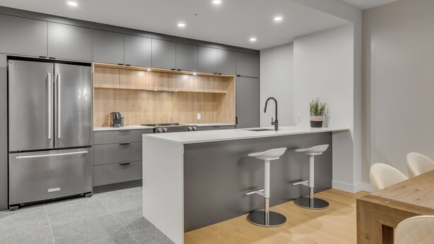 A modern kitchen with grey cabinets, a stainless steel refrigerator, a wooden countertop, and a central island with bar stools.