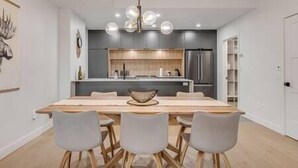 Eine moderne Küche mit einer zentralen Kochinsel, einem Essbereich mit einem Holztisch und vier Stühlen sowie einer Pendelleuchte.