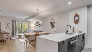 Eine moderne Küche mit Kochinsel, ein Essbereich mit Tisch und Stühlen sowie ein Wohnzimmer mit Sofa.