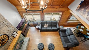 A spacious loft-style room with a stone fireplace, a piano, a large gray sofa, and a dining table with chairs.
