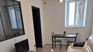 A living room with a sofa, a TV, a dining table, and a small round table with a vase. - L'Atelier T2 Cosy on the first floor (Saint-Gaudens)