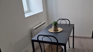 A dining area with a table and chairs, a small plant on the table, and a window providing natural light. - L'Atelier T2 Cosy on the first floor (Saint-Gaudens)