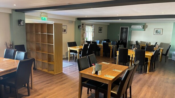 Un grand espace dédié à la salle à manger, avec plusieurs tables et chaises, une bibliothèque en bois et un panneau indiquant la sortie.