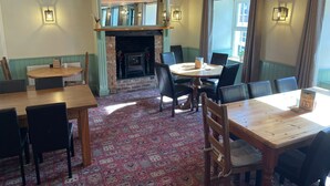 Un coin repas chaleureux avec une cheminée en briques, des tables et des chaises en bois.