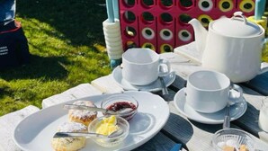 Un coin pique-nique avec une théière blanche, des tasses, des soucoupes et une assiette contenant des scones et de la confiture.