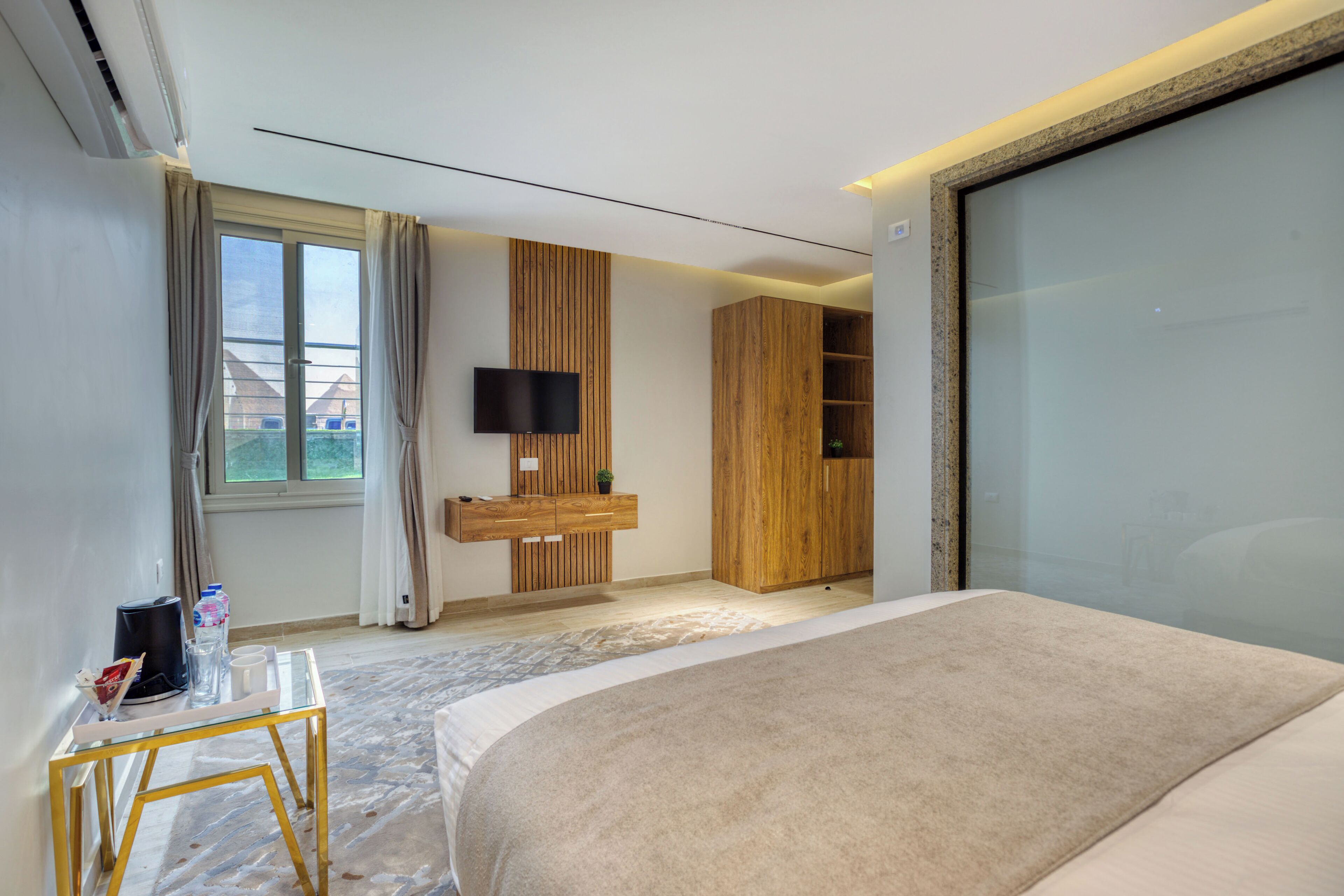 Een moderne hotelkamer met een groot bed, een aan de muur bevestigde televisie, een houten garderobe en een douchecabine van glas.