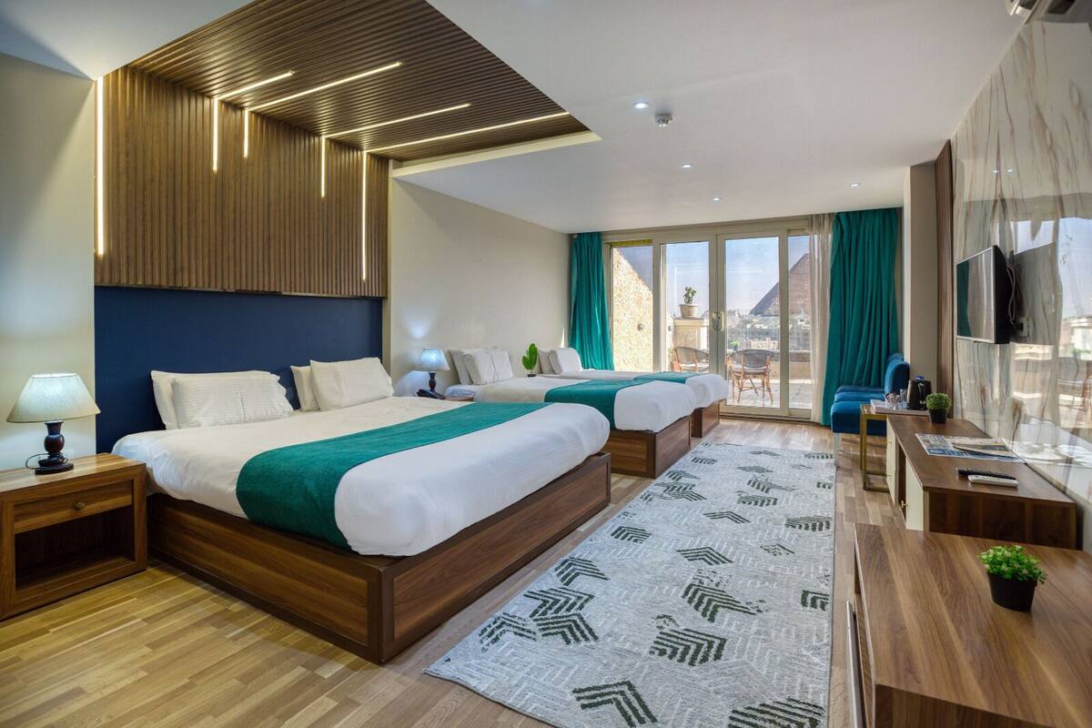 Una habitación de hotel moderna con dos camas, un ventanal grande, un balcón y un escritorio de madera.