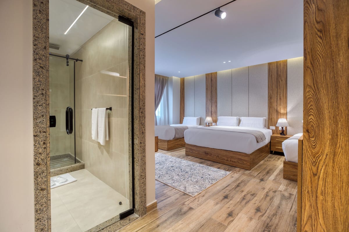 Un dormitorio moderno con cabina de ducha de vidrio, suelo de madera y una cama grande con mesita de noche.