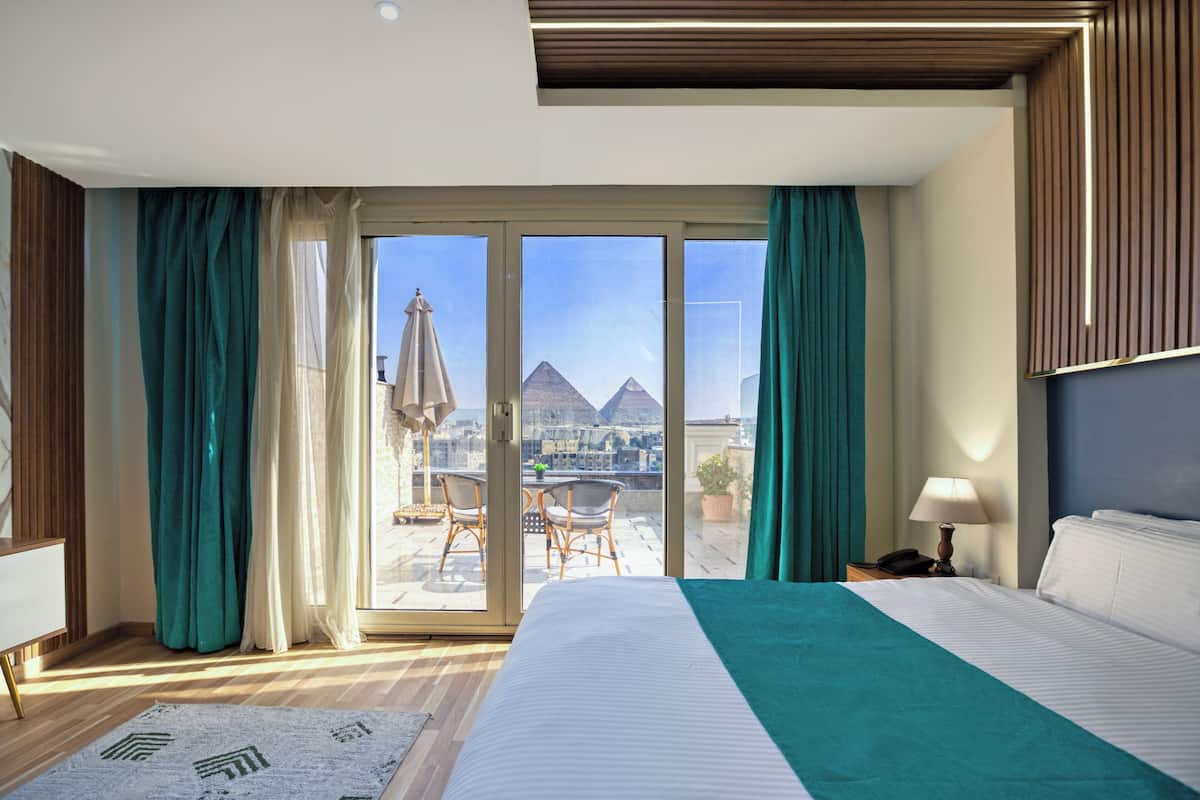 Habitación de hotel con una cama grande, vistas a las pirámides y un balcón con sillas y una mesa.